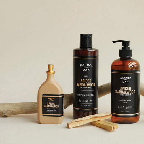 Three amber bottles of men's soap products on a white background. Arranged with two palo santo sticks and a branch in the background. 