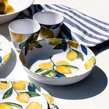 Load image into Gallery viewer, White melamine serving bowl with a yellow lemon and green leaf interior pattern, displayed on a white surface with matching plates and cups, and a blue and white stripe napkin.  