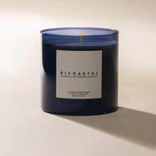 Load image into Gallery viewer, Poured NY Bicoastal candle in blue glass vessel, displayed on a white surface. 