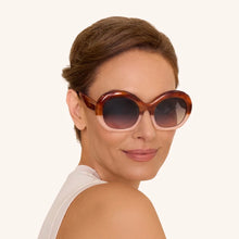 Load image into Gallery viewer, Daria Mahogany Petal Sunglasses worn by model, round polycarbonate frames with two-tone warm brown and petal pink split color, and dark gradient lenses, close-up portrait against a white background. 