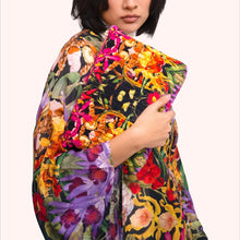 Load image into Gallery viewer, Botanical Kaleidoscope Quilted Velvet Washbag, model wearing a matching kimono holding a rectangular bag with multicolored rainforest pattern, showcasing its quilted finish, hot pink trim, and gold-tone zipper against a white background. 