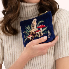 Load image into Gallery viewer, Person wearing a cream-colored ribbed short-sleeved turtleneck holding a royal blue velvet mini pouch embroidered with a brown, gold, and white owl perched on a wood stump among red and white mushrooms and green ferns. Finished with a gold zipper. Against a white background.  
