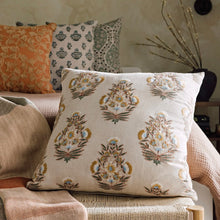 Load image into Gallery viewer, Tansy Pillow, cotton linen blend pillow with block print floral pattern and embroidered embellishments in blue, gold, and brown on a cream background, shown on a chair with patterned pillows in the background. 