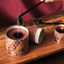 Load image into Gallery viewer, Terra Tabac Vanity Tin Candle, terracotta-toned floral tin candles with brown wax displayed on wood surface, with one recently extinguished full-size candle, one matching travel-size lit candle, lid beside candle, black wick trimmer and smoking candle snuffer in styled setting. 