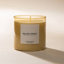 Load image into Gallery viewer, Pour NY Mellow Pomelo candle with cream wax in translucent golden glass vessel on a white surface.  