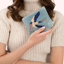 Load image into Gallery viewer, Person wearing a cream-colored ribbed short-sleeved turtleneck holding a light blue velvet mini pouch embroidered with a blue and white swallow in flight, carrying pink flowers and detailed with gold sequins, beads, and blue stitching. Against a white background. 