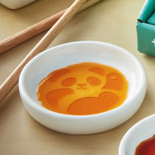 Load image into Gallery viewer, Secret Sauce Dish round white ceramic sauce dish with single embossed panda design revealed by sauce, shown on light surface with chopsticks and packaging in background.  