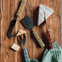 Load image into Gallery viewer, Mosaic cheese knife set of four with stainless steel blades and various floral block print patterned handles, glossy finish, displayed on a wooden surface with cheese wedge slices and green fabric. 