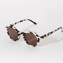 Load image into Gallery viewer, Georgie Cosmic Cowboy Sunglasses, round sunglasses with black, cream, and brown marbled frames, dark brown tinted lenses, and 100% UVA and UVB protection shown at angled side view against white background. 