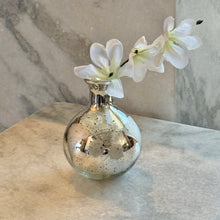 Load image into Gallery viewer, Silver Mercury Glass Etched Bud Vase, globe-shaped silver mercury glass etched bud vase with a narrow flanged neck, displayed with a white floral stem on a light stone surface against a gray marble background. 