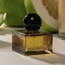 Load image into Gallery viewer, Pour NY Mellow Pomelo square glass parfum bottle with amber liquid, black round cap, and green pomelo fruit on a light surface. 