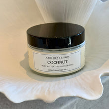 Load image into Gallery viewer, Archipelago Coconut body butter in clear jar with black lid, displayed on a white shell-shaped bowl.