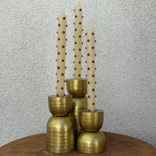 Load image into Gallery viewer, Three unlit white taper candles with metallic red polka dots in gold- looking candle holders of various sizes. On a brown wooden table top. Against a white textured background.   