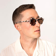 Load image into Gallery viewer, Georgie Cosmic Cowboy Sunglasses, model wearing round sunglasses with black, cream, and brown marbled frames and dark brown tinted lenses against white background. 