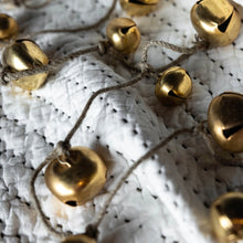 Load image into Gallery viewer, Jingle Bell Garland, close-up of small and large round brass jingle bells tied along brown twine and draped across a white textured knit blanket with black stitched accents. 