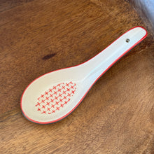 Load image into Gallery viewer, White stoneware Geo soup spoon with red rim and repeating cross interior pattern, displayed on a wooden surface.