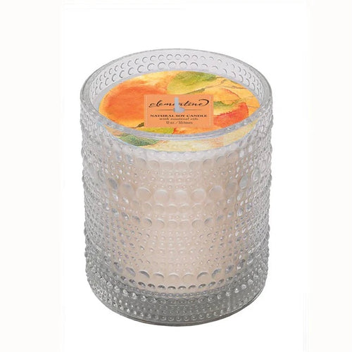 Candle in a bubble textured clear glass holder with an orange and green decorative label on a white background