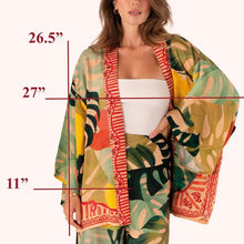 Load image into Gallery viewer, Exotic Leaves Kimono Jacket, lightweight open-front kimono with tropical leaf print in dark green, beige, coral, yellow, and teal with red patterned trim, shown on model with coordinating matching print pants and measurement guide overlay, against white background. 