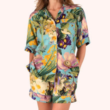 Load image into Gallery viewer, Spring Flora Pajama Set, short-sleeve collared button-up top and matching shorts with iris and daffodil floral print in purple, yellow, cream, and green on light blue background, displayed on model against white background.