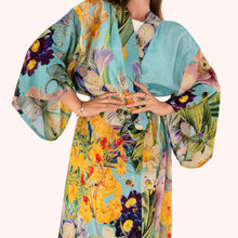 Load image into Gallery viewer, Spring Flora Kimono Gown worn by model, lightweight fabric with large floral pattern in yellow, green, and purple tones on a turquoise-blue background, tie belt, wide sleeves, against a white background. 