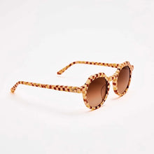 Load image into Gallery viewer, Georgie Toasted Moxie Checkered Sunglasses, angled view of round acetate sunglasses with UVA/UVB protection, gradient amber-brown lenses, and red, cream, brown, and golden yellow checkered frames against white background. 