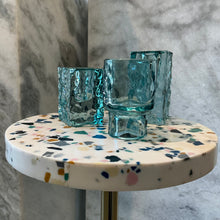Load image into Gallery viewer, Hammered Glass Taper Holder, three aqua blue hammered glass candle holders displayed on multicolor terrazzo pedestal against gray marble background. 