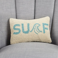 Load image into Gallery viewer, Surf Hook Pillow, rectangular hooked wool throw pillow with a cream background and turquoise blue "SURF" lettering, featuring a stylized wave forming the letter "R," displayed on a light light gray upholstered chair.  