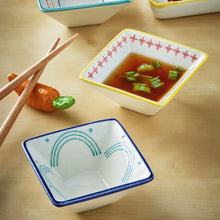 Load image into Gallery viewer, Square stoneware Geo dish with blue, yellow, and teal rims featuring clean lines, one filled with broth and garnishes on a wood surface. 