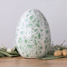 Load image into Gallery viewer, Rustic ceramic egg figurine with green floral, botanical, and rabbit pattern, displayed on a wood surface. 
