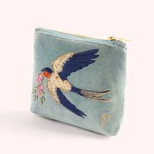 Load image into Gallery viewer, Light blue velvet mini pouch embroidered with a white and blue swallow in flight carrying pink flowers. Detailed with gold beads, sequins, and blue stitching. Finished with a gold zipper. A gold embroidered cursive &quot;P&quot; in the lower right corner. Displayed against a white background.  