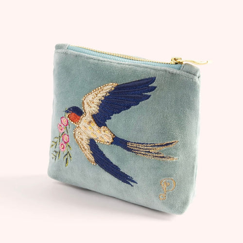 Light blue velvet mini pouch embroidered with a white and blue swallow in flight carrying pink flowers. Detailed with gold beads, sequins, and blue stitching. Finished with a gold zipper. A gold embroidered cursive 