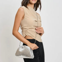 Load image into Gallery viewer, Model wearing the silver woven vegan-leather half-moon crossbody bag with a silver chain strap, styled with a beige sleeveless top and black pants against a white background. 