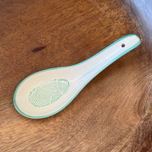 Load image into Gallery viewer, White stoneware Geo Soup spoon with teal rim and curved line interior pattern, displayed on a wooden surface.