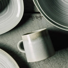 Load image into Gallery viewer, Aquarius Sage stoneware mug with reactive glaze, angled view on a stone surface with matching dinnerware.