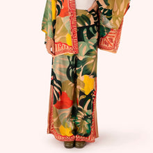Load image into Gallery viewer, Exotic Leaves Wide Leg Trousers worn by model, lightweight fabric with large tropical leaf pattern in green, yellow, and coral tones, red patterned trim, wide leg silhouette, paired with matching kimono, against a white background.  