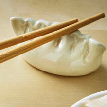 Load image into Gallery viewer, Glossy white dolomite chopstick rest shaped like a dumpling with ruffled top, displayed with wooden chopsticks on a neutral background.  
