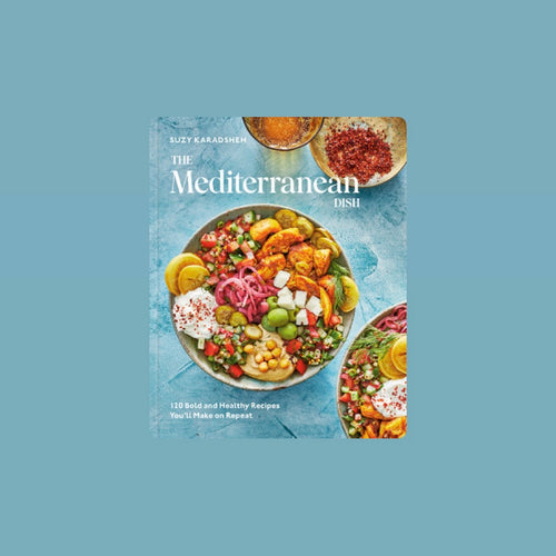 Book cover of The Mediterranean Dish by Suzy Karadsheh featuring a colorful bowls filled with hummus, olives, pita, pickled onions, cucumbers, tomatoes, and grilled chicken on a blue surface with white lettering. Book is against a light blue background.   