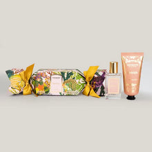 Load image into Gallery viewer, Granado Nostalgia scented cracker with tropical floral packaging and yellow ribbon bows beside Nostalgia perfume in a clear glass bottle with gold cap and hand cream in a peach tube with black cap on a white background. 