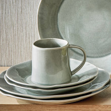 Load image into Gallery viewer, Hudson ceramic mug with reactive glaze slate finish and organic shape, displayed stacked with coordinating plates and bowl on a wooden surface. 