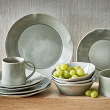 Load image into Gallery viewer, Hudson ceramic salad plate with reactive glaze slate finish and organic shaped rim, displayed stacked with coordinating plates, bowls, and mug on a wooden surface. 