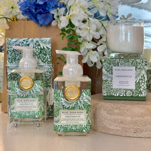 Load image into Gallery viewer, Michel Design Works Greenhouse collection with foaming shea butter hand soap pump bottles, double compartment metal caddy with paper guest towels, and candle in clear glass vessel on matching green box atop a stone riser, all featuring white botanical pattern on green background displayed with floral backdrop. 