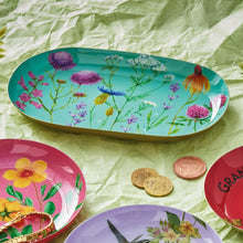Load image into Gallery viewer, Wildflowers Metal Trinket Tray, oval aqua metal trinket tray with colorful wildflower illustrations, displayed with assorted coordinating floral trinket dishes, gold coins, and jewelry on light green crinkled surface. 