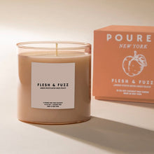 Load image into Gallery viewer, Poured NY Flesh &amp; Fuzz candle in clear glass vessel with peach-toned wax, displayed on a white surface with coordinating peach-colored packaging box in background. 