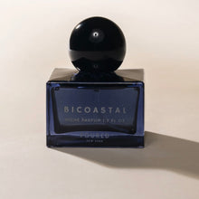 Load image into Gallery viewer, Poured NY Bicoastal parfum in blue glass bottle with round black cap, displayed on a white surface. 