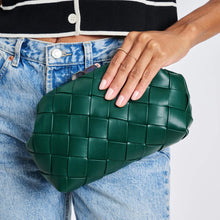 Load image into Gallery viewer, Model holding a woven forest-green vegan-leather crossbody bag while wearing light wash jeans and a black short-sleeve top with white accents against a white background. 