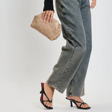 Load image into Gallery viewer, Model holding a woven beige vegan-leather crossbody bag while wearing relaxed high-waisted jeans and black heeled sandals against a white background. 