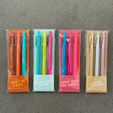 Load image into Gallery viewer, Four packs of colorful Jotter gel pens- &quot;Don&#39;t Be a Dick&quot; in an orange sleeve, &quot;Everything is Fine&quot; in a baby blue sleeve, &quot;Jesus Take the Wheel&quot; in a pink sleeve, and &quot;Stay Golden&quot; in an beige sleeve- arranged in a row on a gray textured surface.