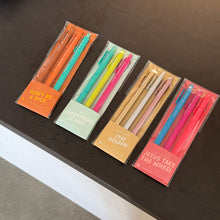 Load image into Gallery viewer, Four packs of colorful Jotter gel pens- &quot;Don&#39;t Be A Dick&quot; in an orange sleeve,  &quot;Everything Is Fine&quot; in a baby blue sleeve, &quot;Stay Golden&quot; in a beige sleeve, and &quot;Jesus Take The Wheel&quot; in a pink sleeve- displayed side by side on a dark surface. 