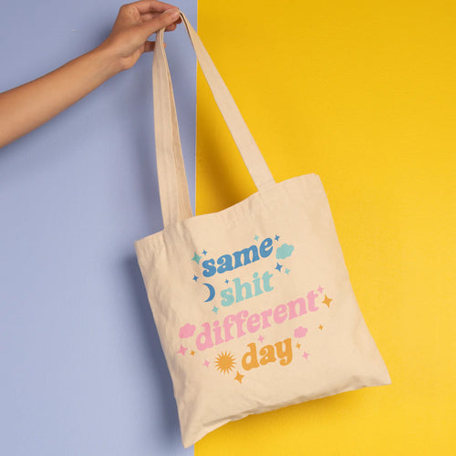 White canvas tote bag with long handles, held by a person's hand, printed with the phrase 