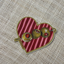 Load image into Gallery viewer, Heart-shaped stickers with pink-and-red stripes and green olive illustrations, displayed on a tan fabric surface. 